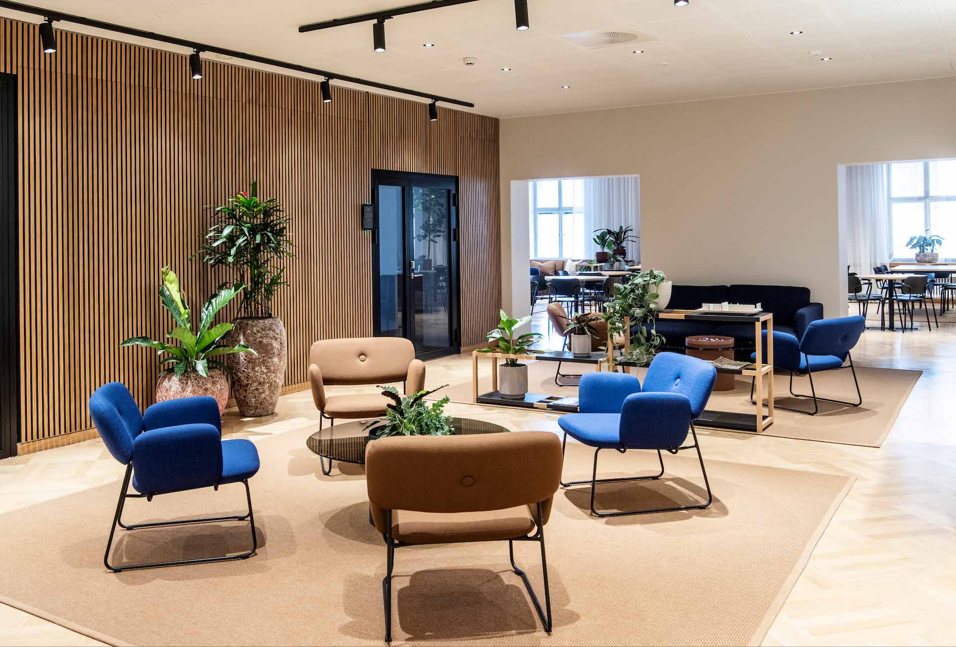 Toimiston suuri aulatila, jossa ruskean ja sinisen sävyisiä nojatuoleja ja viherkasveja